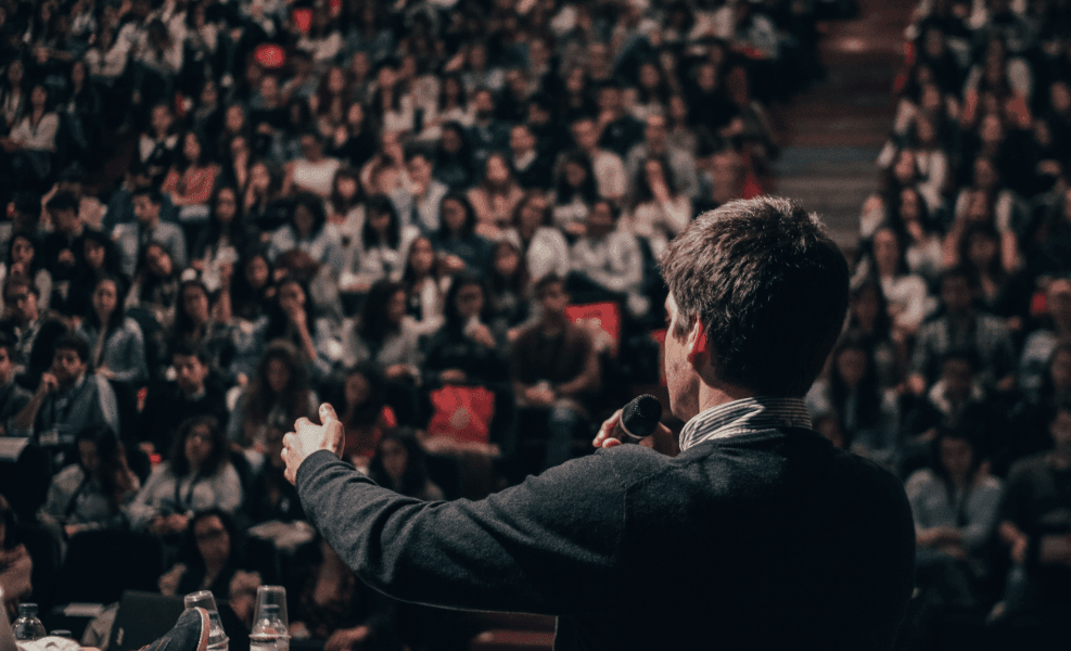 A man speaks to an audience from a microphone on a stage.
