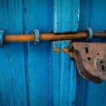 A blue wooden door secured shut thanks to a bolt and padlock.